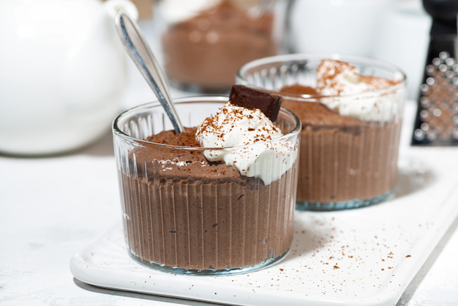 Two glass ramekins of chocolate crémeux with whipped cream.