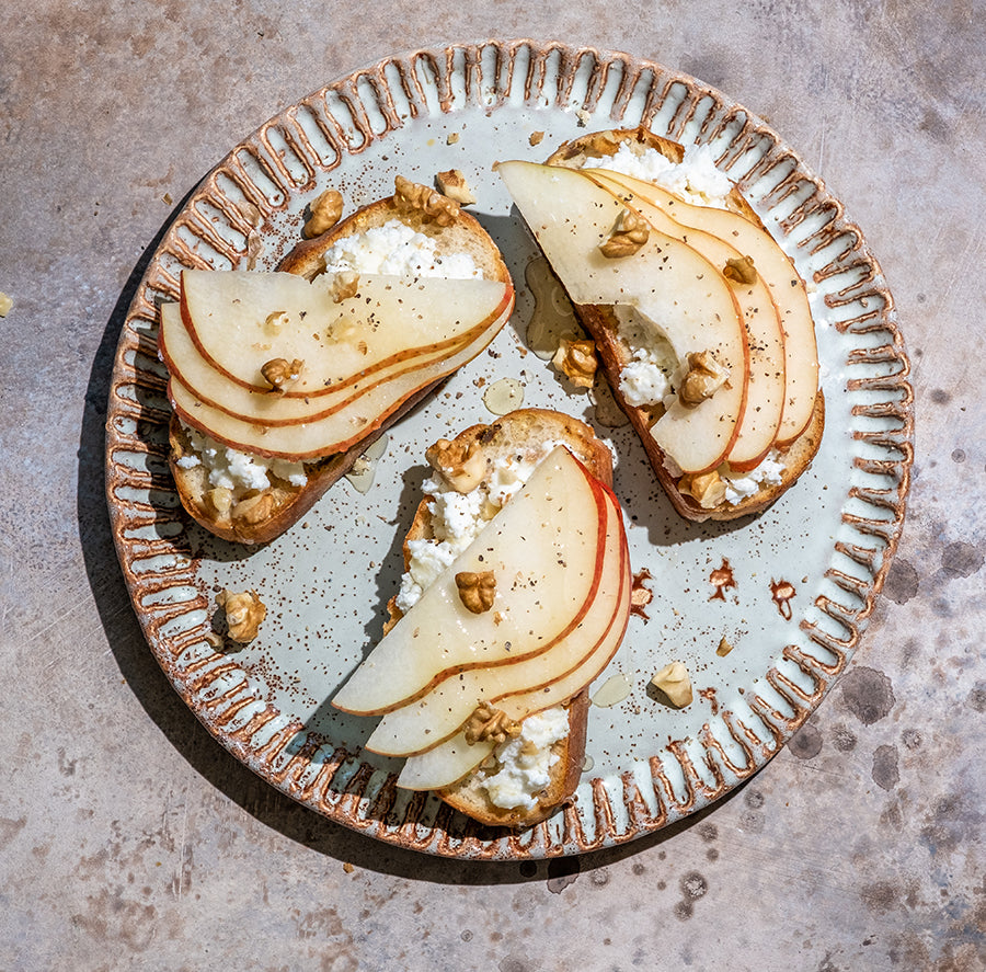 Three slices of toast with pear slices, goat cheese, and nuts on a decorative plate.